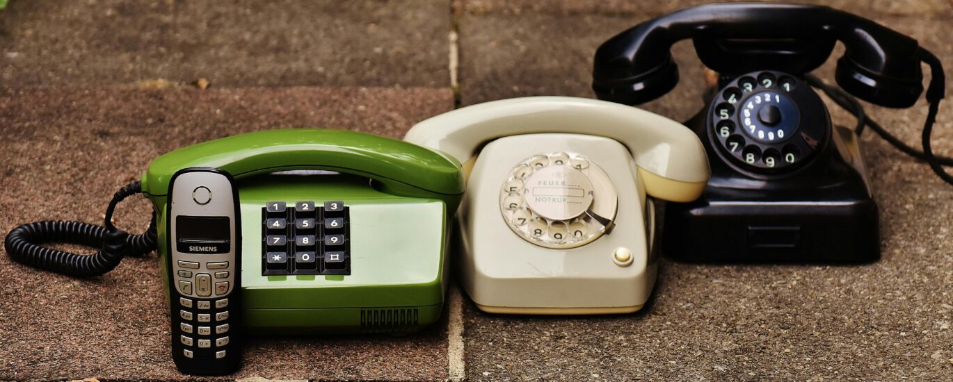 A variety of antique, vintage, and modern telephones displayed on pavement.